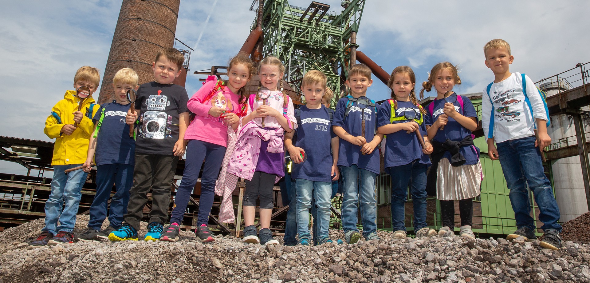 Eine Gruppe von Kindern steht in einer Reihe vor einem Hochofen.