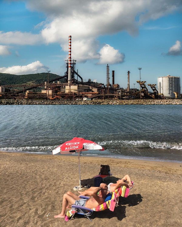 Fotomontage eines Pärchens, das ein Sonnenbad vor der Kulisse einer Industrieanlage nimmt.