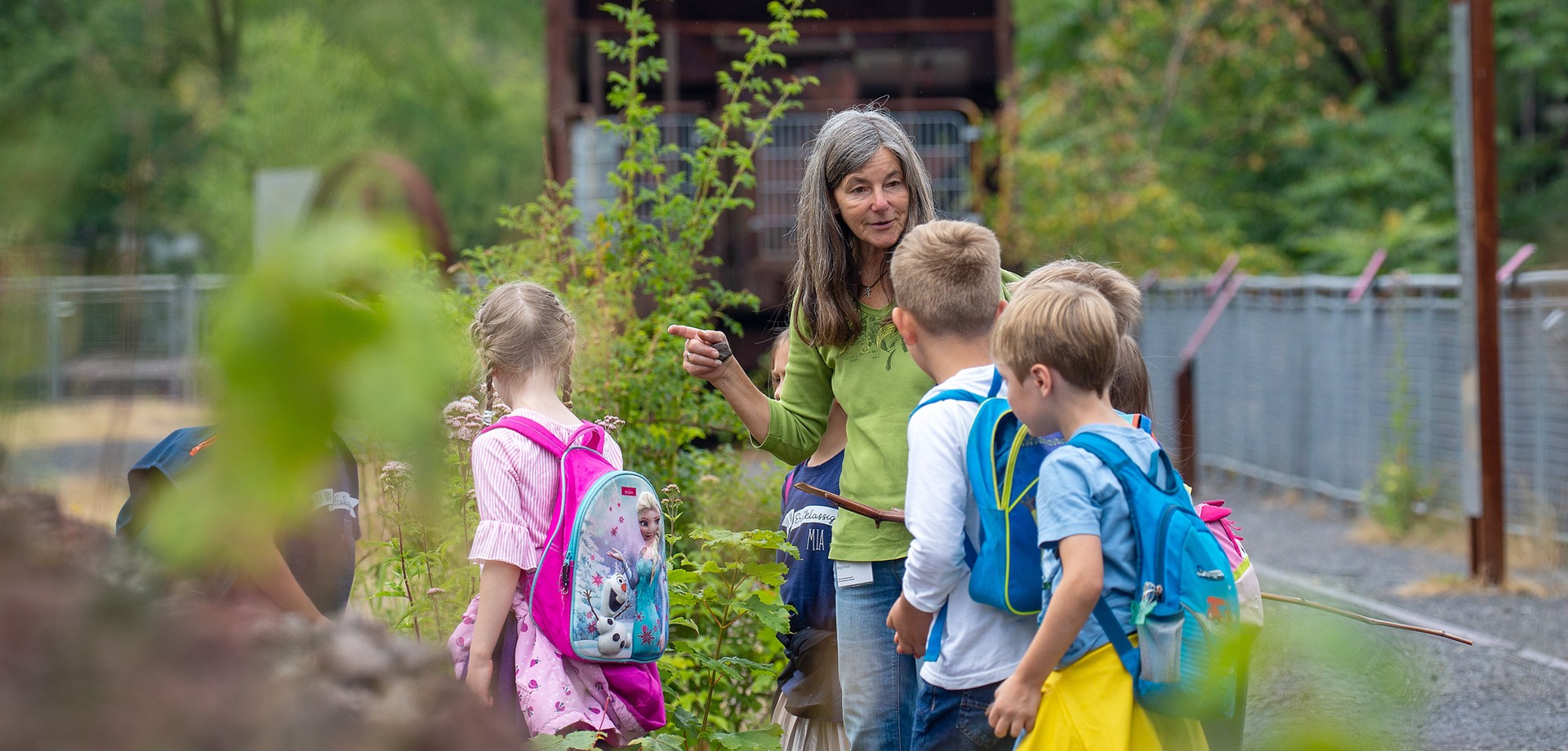 Kinder umgeben von grüner Natur mit einer Naturführerin auf dem ehemaligen Industriegelände
