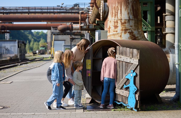 Kinder und Erwachsenen vor einem Holzfass auf dem Gelände der Henrichshütte