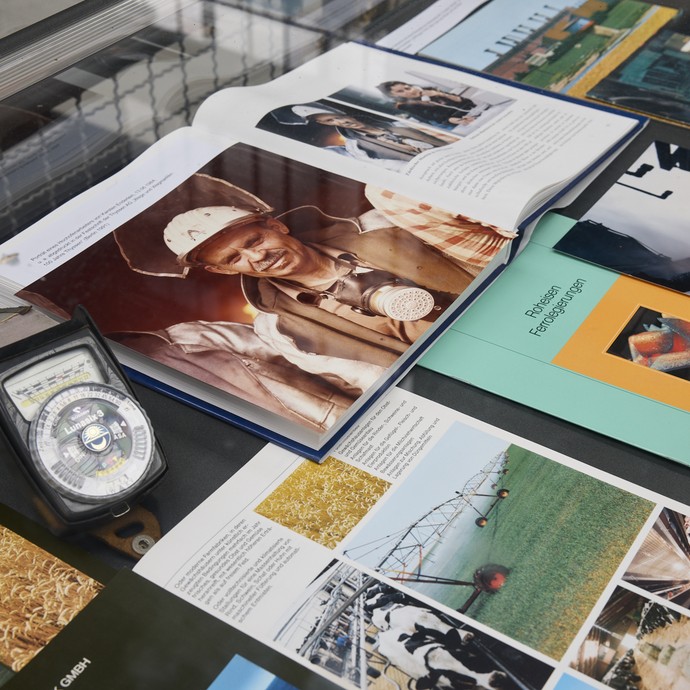 Kataloge, Fotografien und Gegenstände in einer Vitrine ausgelegt (vergrößerte Bildansicht wird geöffnet)