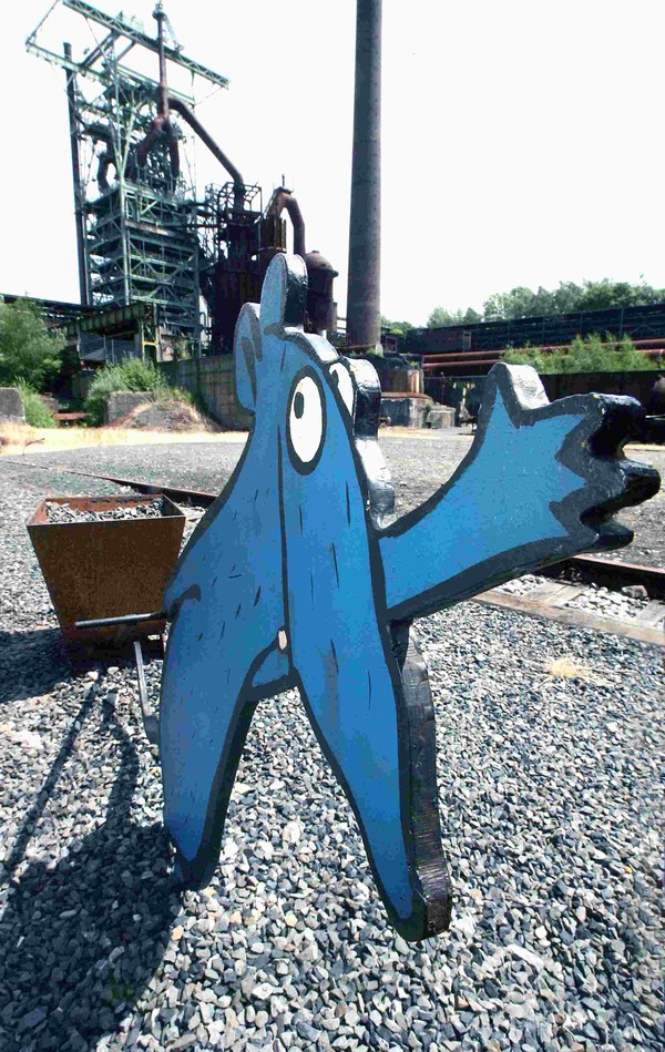 Winkende blaue Museumsratte aus Stahl. Im Hintergrund der Hochofen.