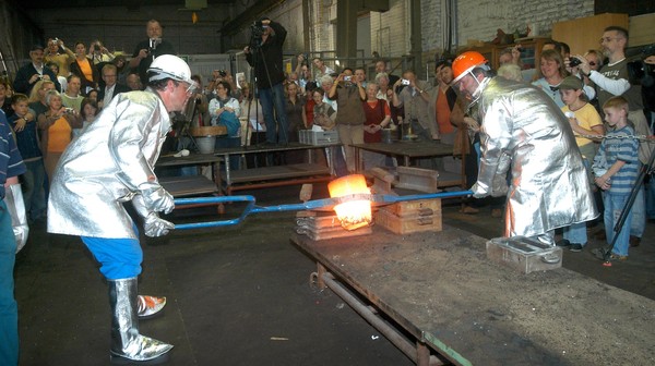Flüssiger Stahl wird von zwei Hüttenmitarbeitern in eine neue Form gebracht.