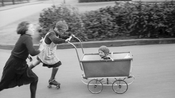 Drei Kinder spielen mit Rollschuhen und Kinderwagen.