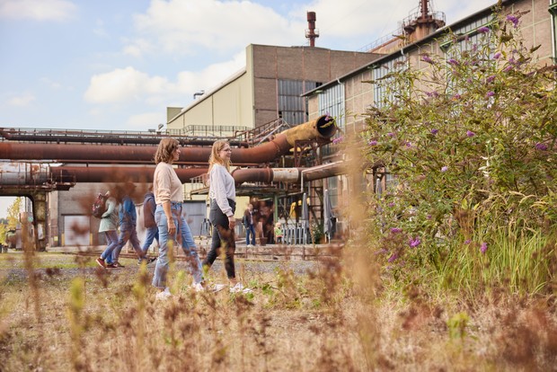 Zwei Frauen spazieren neben Pflanzen und Sträucher die auf der Indsutriebrache wachsen