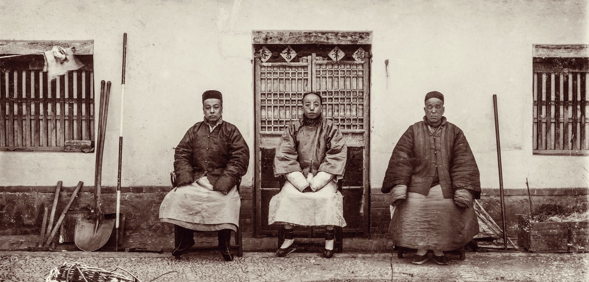Drei Männer in historischer chinesischer Kleidung sitzen vor einem Gebäude.
