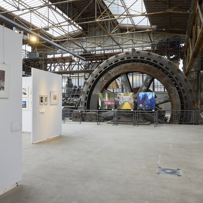 Maschinen der Maschinenhalle umgeben von Bildern der Ausstellung mit Szenen der Industriegeschichte der Region (vergrößerte Bildansicht wird geöffnet)