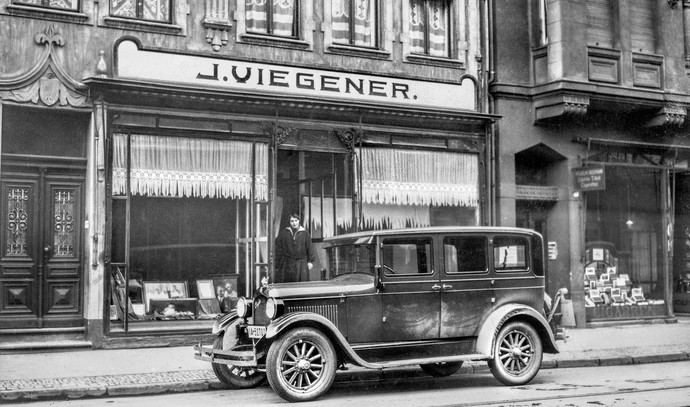 Schwarz-weiß Fotografies eines alten Autos vor einem Ladenlokal.