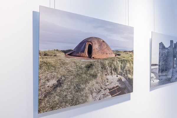 Blick auf eine Fotografie der Ausstellung: Bunkerreste in Dünenlandschaft.
