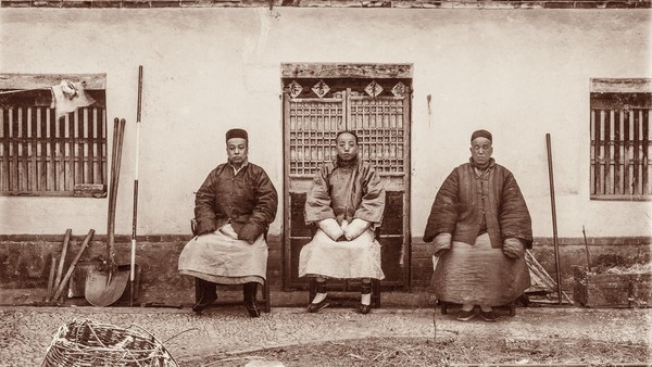Drei Männer in historischer chinesischer Kleidung sitzen vor einem Gebäude.